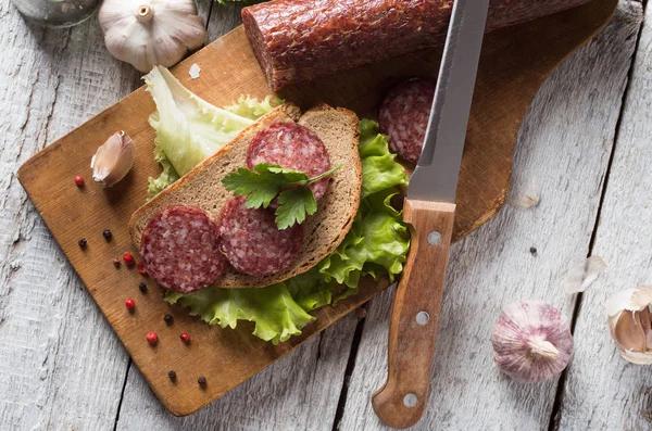 Salami y pan en una tabla de madera — Foto de Stock