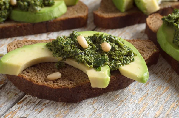 Sandwich con salsa de pesto y aguacate en una tabla de madera —  Fotos de Stock