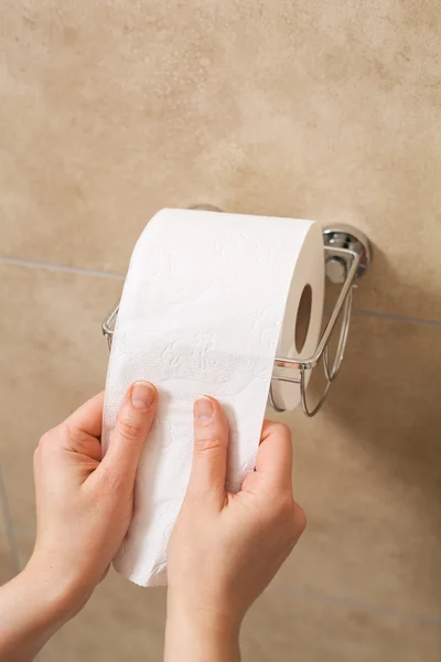 Hand pulling toilet paper roll in holder — Stock Photo, Image