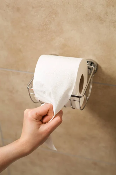 Hand pulling toilet paper roll in holder — Stock Photo, Image