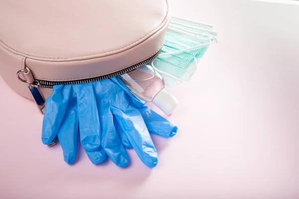 protective medical mask, sanitizer gel and gloves in pink bag. protective measures against virus, bacteria