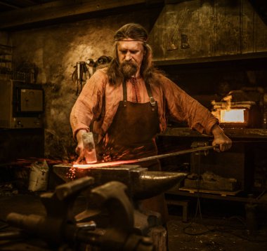 Senior blacksmith forging the molten metal  clipart