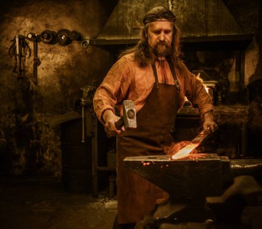 Senior blacksmith forging the molten metal  clipart