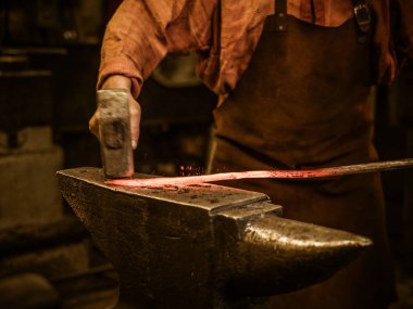 Senior blacksmith forging the molten metal  clipart