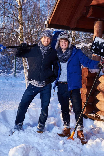 Två vänner skotta snö från gården i vinterstuga — Stockfoto