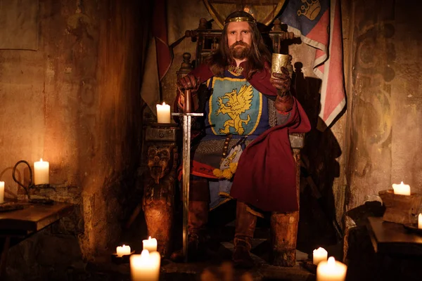 Medieval king on throne in ancient castle interior.