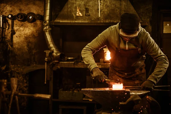 Kovács kefével kezeli az olvadt fém a az üllőt a kovácsmuhelyben — Stock Fotó