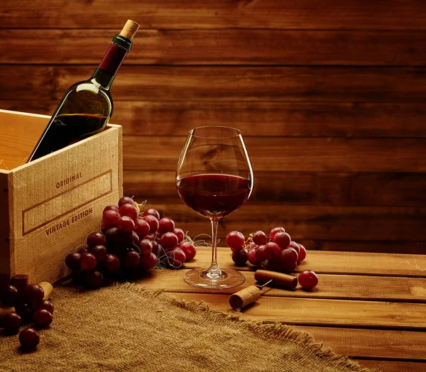 Бутылка, стекло и красный виноград на деревянном столе — стоковое фото