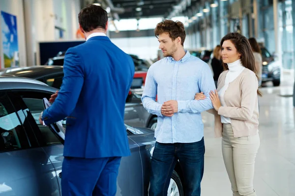 Verkäufer im Gespräch mit einem jungen Paar im Autohaus — Stockfoto