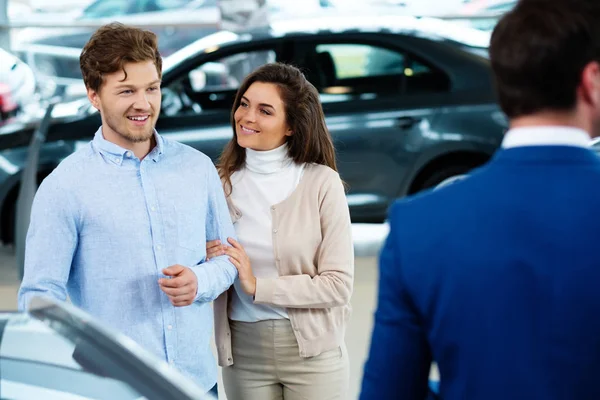 Salesman talking to a young couple at the dealership showroom — Stock Photo, Image