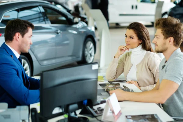 Beautiful young couple reading a booklet at the dealership showroom — Stock Photo, Image