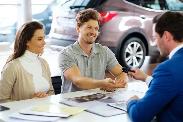 Salesman giving the key of the new car to a young couple — Stock Photo, Image