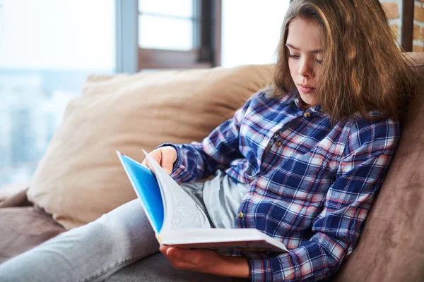 Linda niña leyendo libro en un sofá —  Fotos de Stock