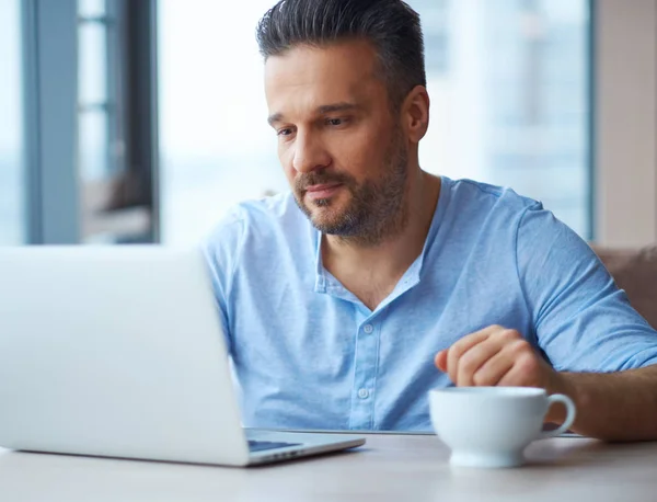 Snygg man med kopp kaffe med hjälp av laptop hemma — Stockfoto