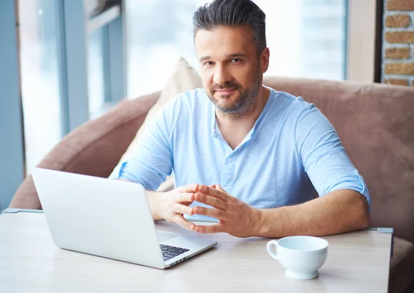 Przystojny człowiek z filiżanką kawy przy użyciu laptopa w domu — Zdjęcie stockowe