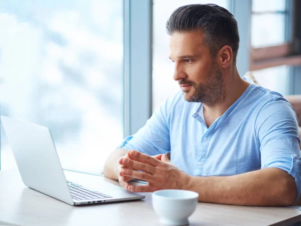 Bello uomo con tazza di caffè utilizzando il computer portatile a casa — Foto Stock