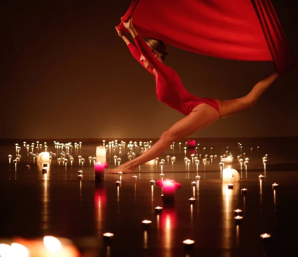 Rapariga em vermelho realizando ioga aérea em luzes de vela relaxantes — Fotografia de Stock