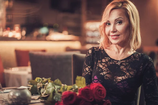 Portrait of beautiful middle aged woman with bouquet of red roses in restaurant — Stock Photo, Image