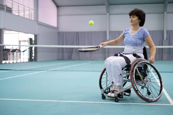 Disabled mature woman on wheelchair playing tennis on tennis court — Stock Photo, Image