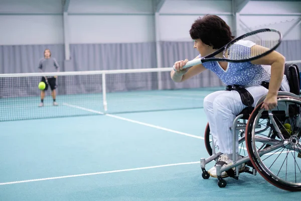 Disabled mature woman on wheelchair playing tennis on tennis court — Stock Photo, Image