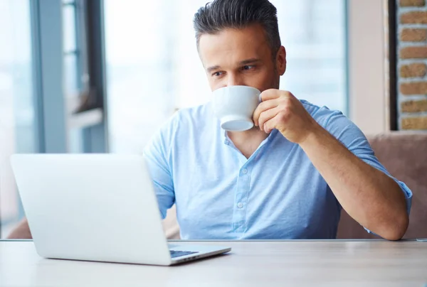 Snygg man med kopp kaffe med hjälp av laptop hemma — Stockfoto