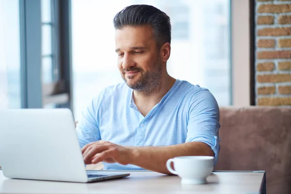 Bel homme avec tasse de café en utilisant un ordinateur portable à la maison — Photo