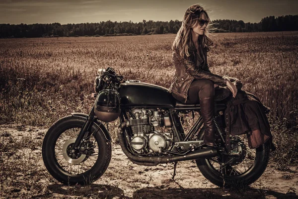 Young, stylish woman on vintage custom cafe racer in field — Stock Photo, Image