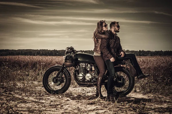 Young, stylish cafe racer couple on vintage custom motorcycles in field — Stock Photo, Image