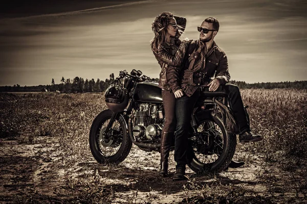 Joven y elegante pareja de corredores de café en motocicletas personalizadas vintage en el campo — Foto de Stock