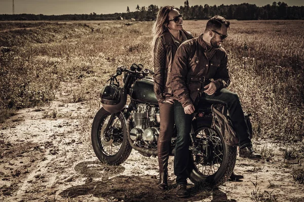 Jovem, elegante casal piloto de café em motocicletas personalizadas vintage em campo — Fotografia de Stock