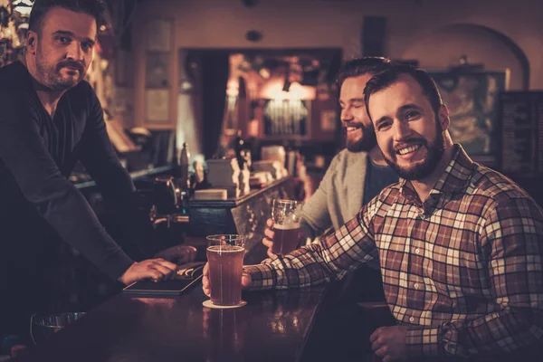 Cheerful old friends drinking draft beer at bar counter in pub. — Stock Photo, Image