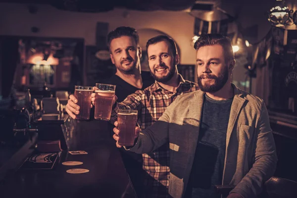 Cheerful old friends drinking draft beer at bar counter in pub.