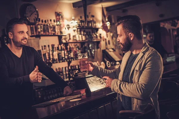 Stilvoller Mann bezahlt Bier mit Karte an Barkeeper in Kneipe. — Stockfoto