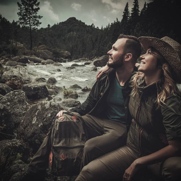 Χαρούμενο ζευγάρι πεζοπόρους συνεδρίασης κοντά ποταμός άγριο βουνό. — Φωτογραφία Αρχείου