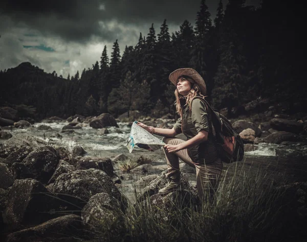 Žena turista, hledání správným směrem na mapě poblíž divoká horská řeka. — Stock fotografie