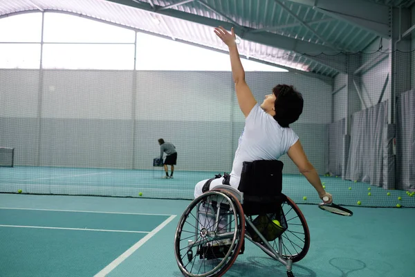 Disabled mature woman on wheelchair playing tennis on tennis court. — Stock Photo, Image