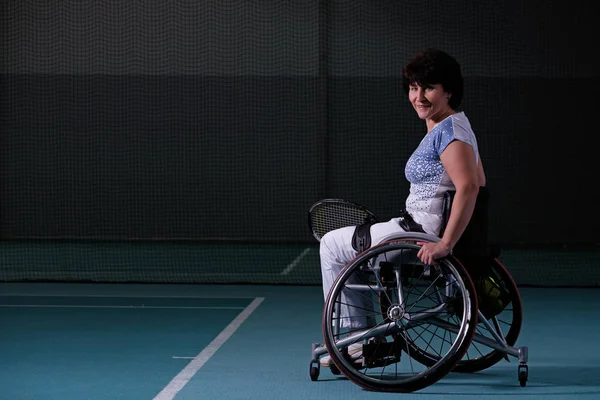 Disabled mature woman on wheelchair playing tennis on tennis court. — Stock Photo, Image