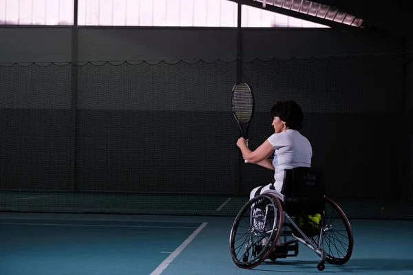 Disabled mature woman on wheelchair playing tennis on tennis court. — Stock Photo, Image