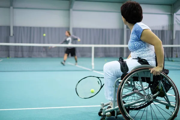 Disabled mature woman on wheelchair playing tennis on tennis court. — Stock Photo, Image