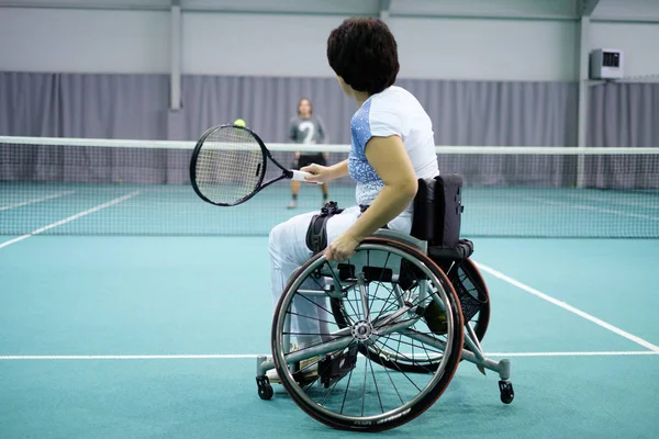 Disabled mature woman on wheelchair playing tennis on tennis court. — Stock Photo, Image