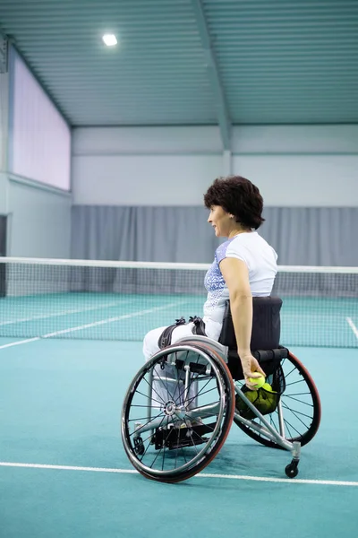 Disabled mature woman on wheelchair playing tennis on tennis court. — Stock Photo, Image