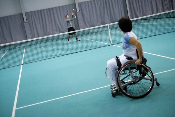 Disabled mature woman on wheelchair playing tennis with a coach — Stock Photo, Image