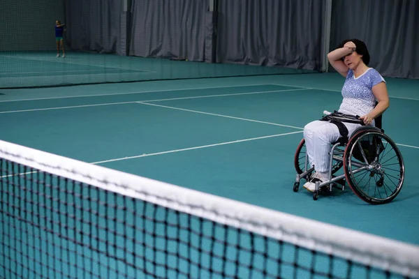 Cansada mujer madura con discapacidad en silla de ruedas en la cancha de tenis . —  Fotos de Stock