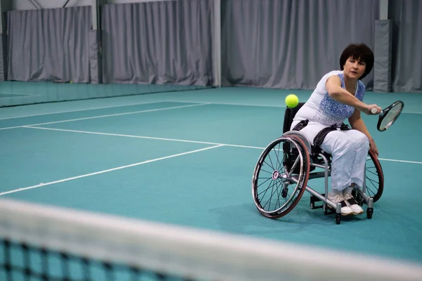 Femme mature handicapée en fauteuil roulant jouant au tennis sur un court de tennis . — Photo