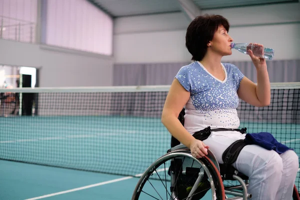 Disabili assetati donna matura sulla sedia a rotelle al campo da tennis . — Foto Stock