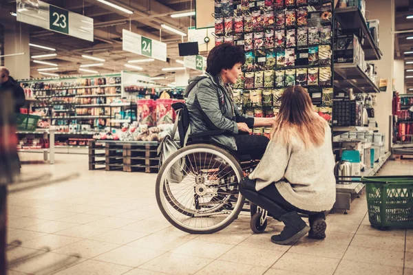 Νεαρό κορίτσι βοηθώντας τα άτομα με ειδικές mothter σε αναπηρική καρέκλα σε ένα πολυκατάστημα — Φωτογραφία Αρχείου