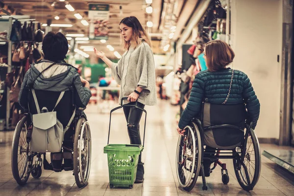 Giovane ragazza che aiuta due donne disabili in sedia a rotelle in un grande magazzino — Foto Stock