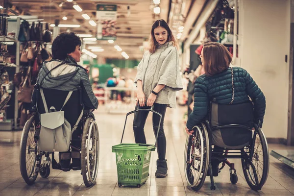 Jong meisje helpen twee vrouwen met een handicap in rolstoel in een warenhuis — Stockfoto