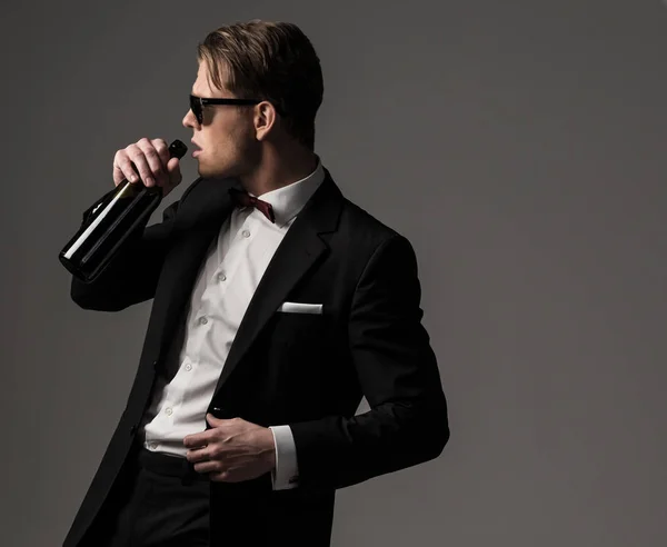 Ostré oblečený muž v černém obleku s lahví vína — Stock fotografie