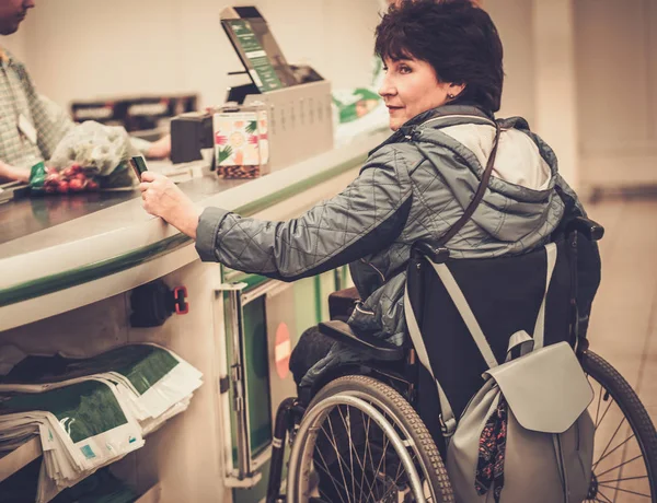 Gehandicapte vrouw in een rolstoel betalen met credit card in een winkel — Stockfoto